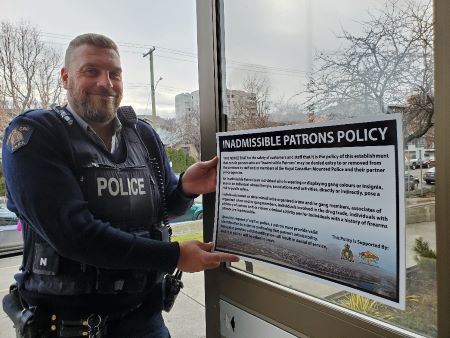 A uniformed police officer holds up an Admissible Patrons Policy in front of a window.  