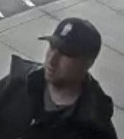 Vue rapprochée d’un homme dans un magasin, portant une casquette de baseball noire, un chandail foncé et une veste foncée.