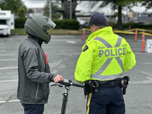 Un agent de la GRC à Richmond, debout à côté d’une personne en trottinette électrique.