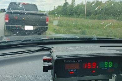 Radar de police affichant une vitesse de la cible de 159 et une vitesse du policier de 98; un camion noir se trouve en arrière-plan.